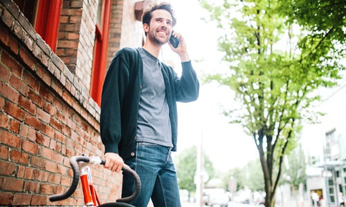 Man on a neighborhood street next to bike talking on his phone and smiling